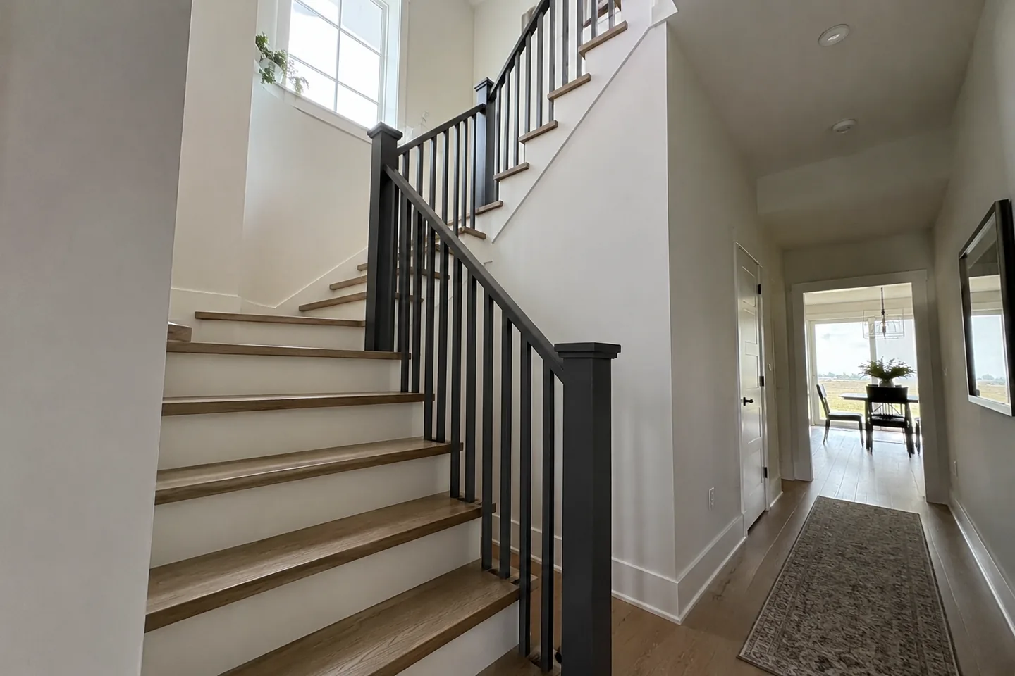Tall warm-white stairwell with timber treads and a charcoal handrail
